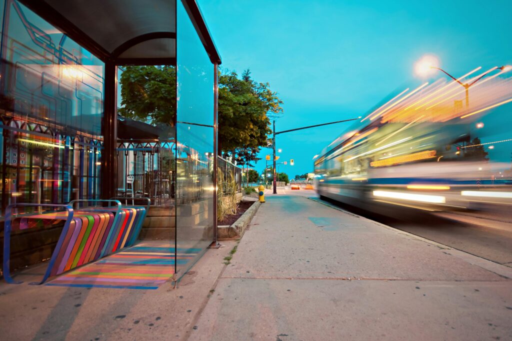 Colorful city bus stop with vibrant benches, blurred motion of a passing bus at dusk.